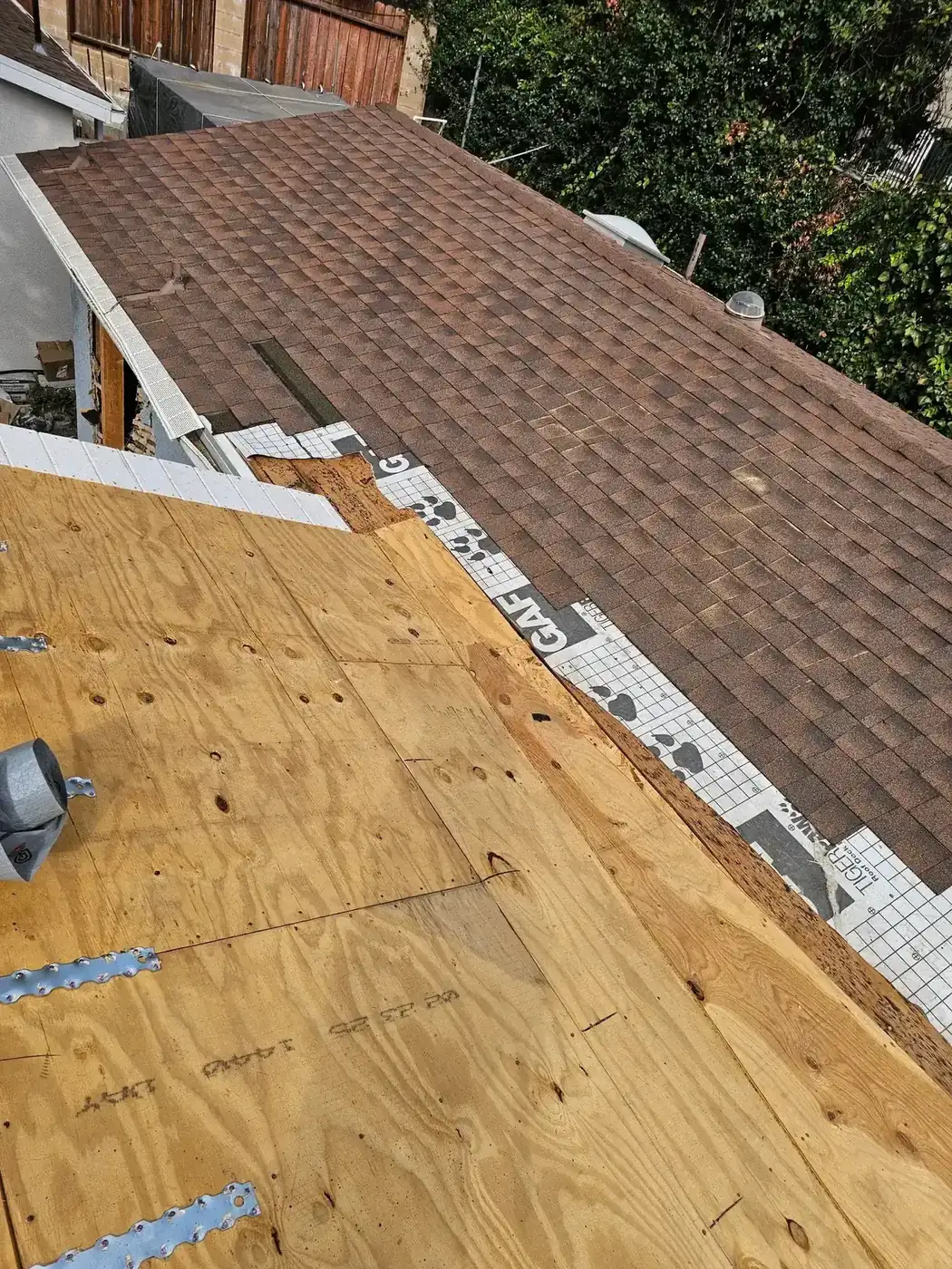 New plywood roof decking on the addition meets the existing shingle roofline where the two structures tie together at PMK's addition-and-remodel project in La Crescenta.