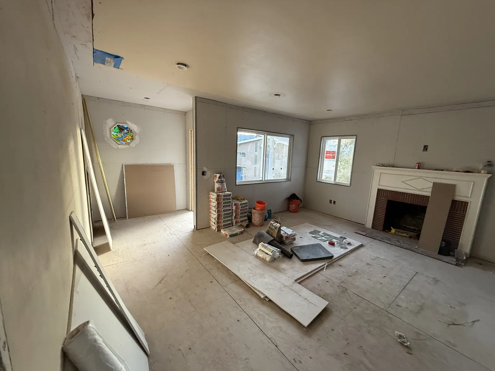 Drywall hung around the original fireplace and the octagonal stained-glass window opening as interior surfaces take shape at PMK's La Crescenta addition-and-remodel project.
