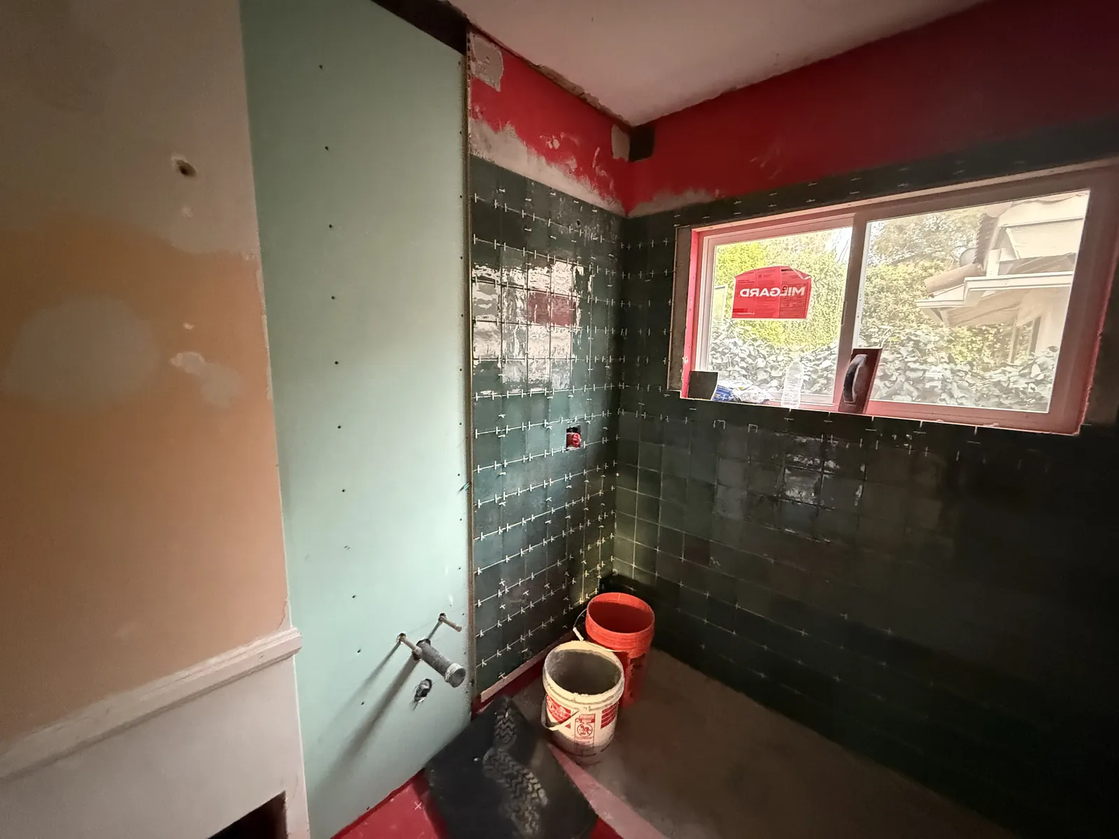 Green square tile is set over red waterproofing membrane in the new bathroom during tile installation at PMK's addition-and-remodel project in La Crescenta.