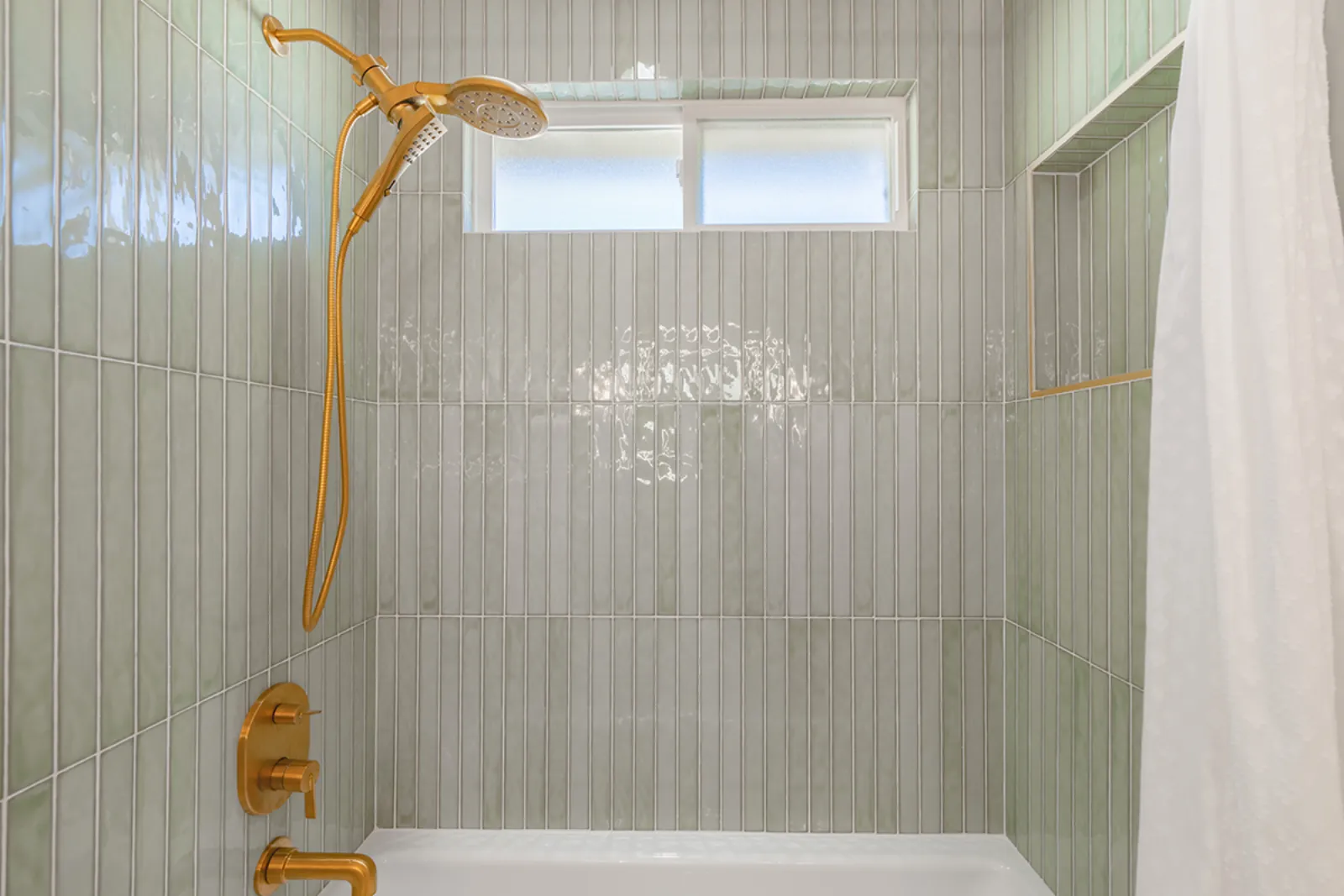 Tiled shower wall with brass fixtures and a built-in niche from a PMK Development bathroom remodel in Burbank