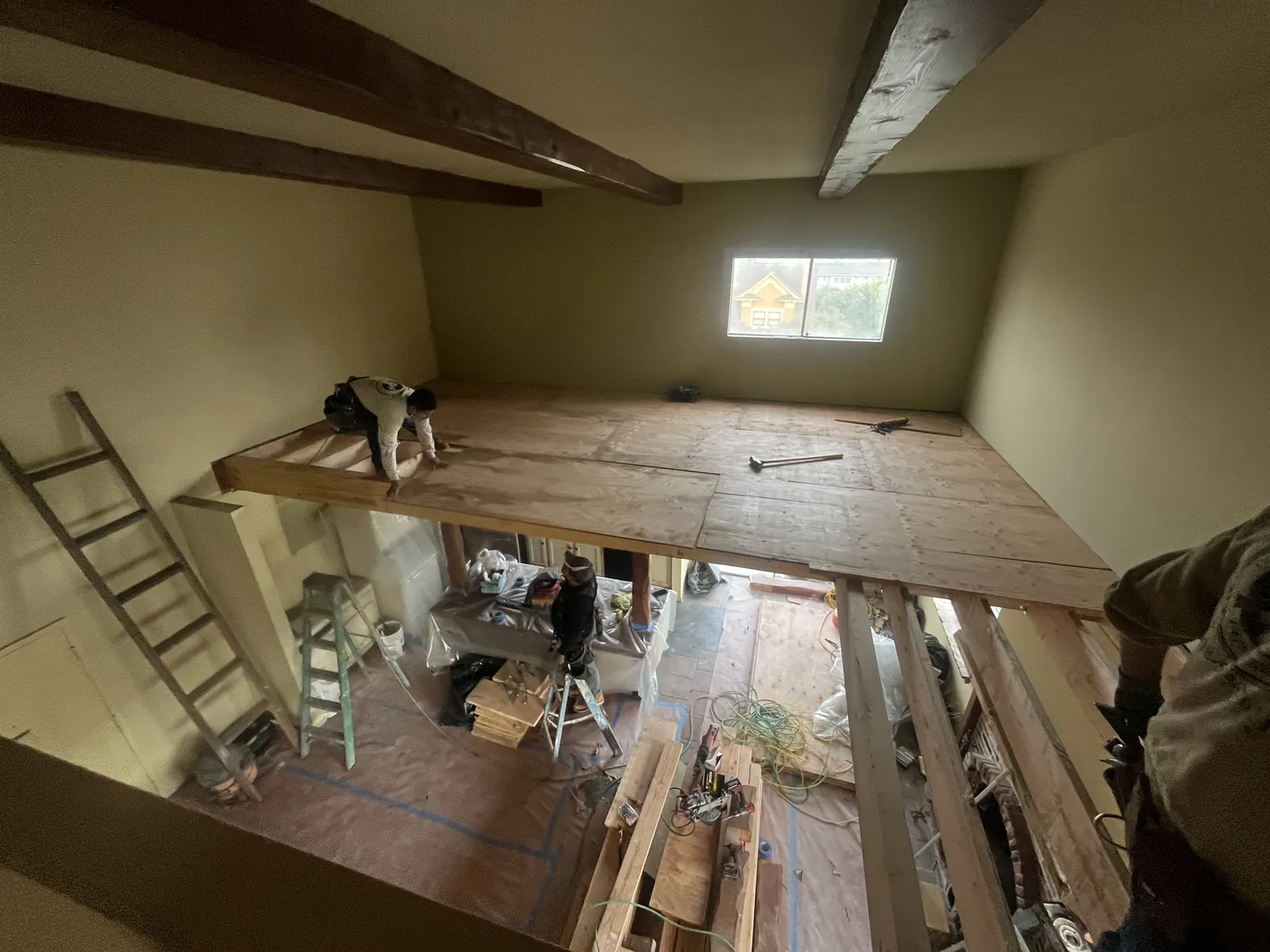 A worker nails down plywood subflooring on a new loft level above an open kitchen during PMK Development's interior remodel on Harvard Blvd in Los Angeles.