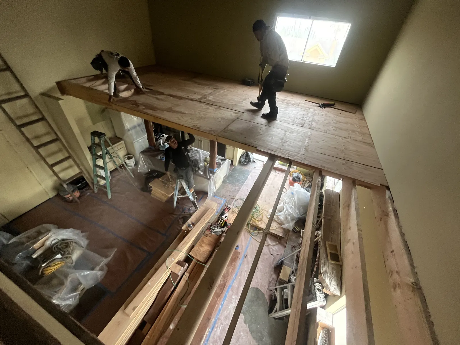 Crew members build out the loft platform and subfloor above exposed floor joists during PMK Development's interior remodel on Harvard Blvd in Los Angeles.