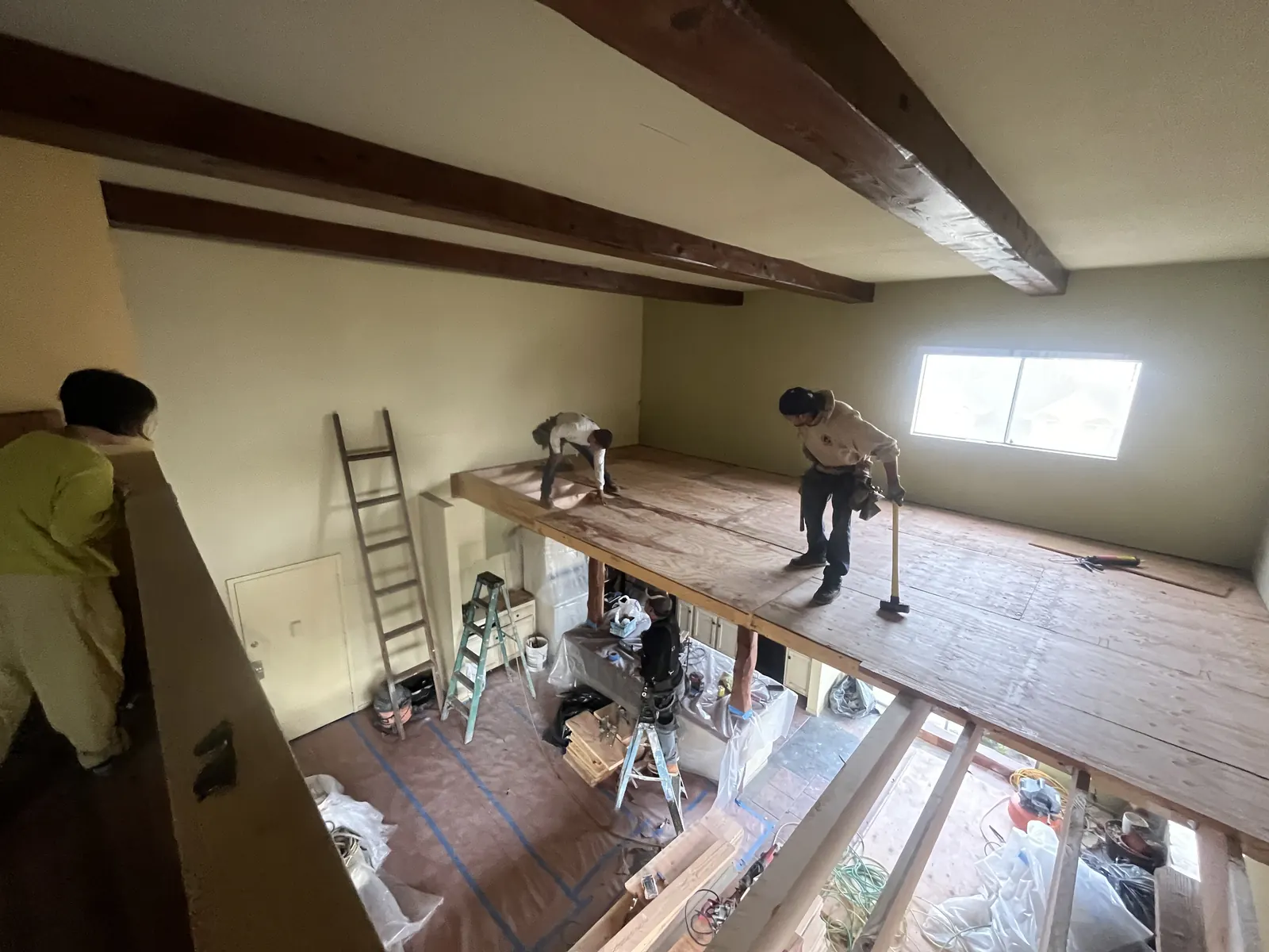 Two crew members work on the new loft subfloor above a plastic-draped kitchen counter during PMK Development's interior remodel on Harvard Blvd in Los Angeles.