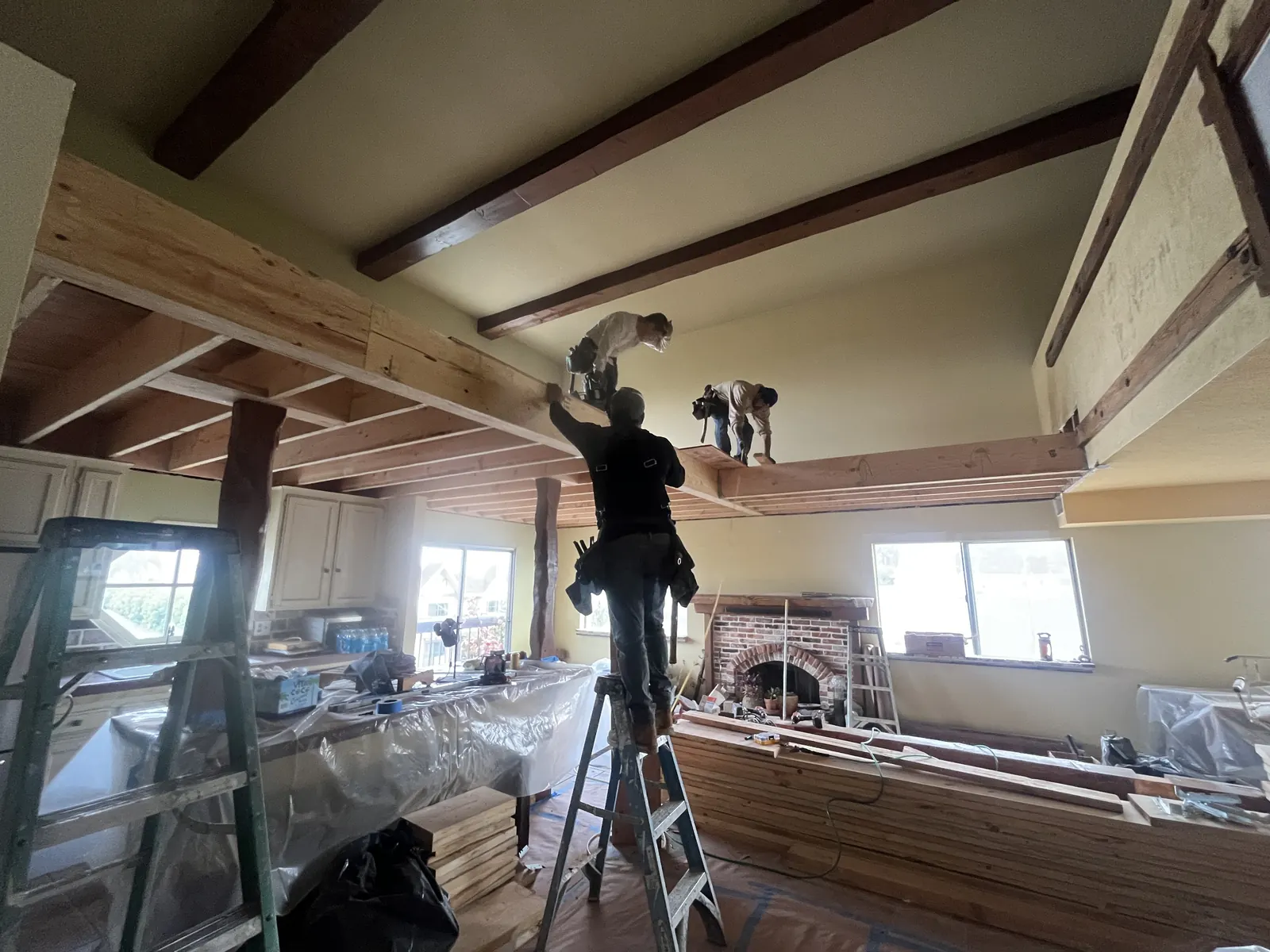 Crew members install structural framing for a new loft level above the great room's brick fireplace during PMK Development's interior remodel on Harvard Blvd in Los Angeles.