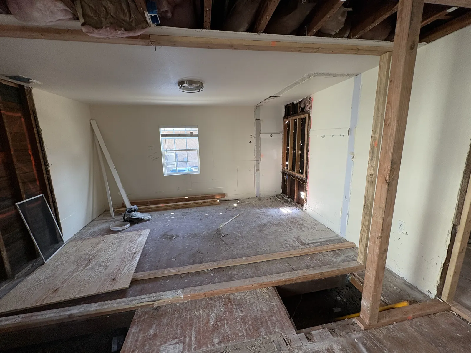 A room taken down to exposed ceiling joists and patched plywood subfloor during PMK's open-concept remodel on Hobart Blvd in Los Angeles.