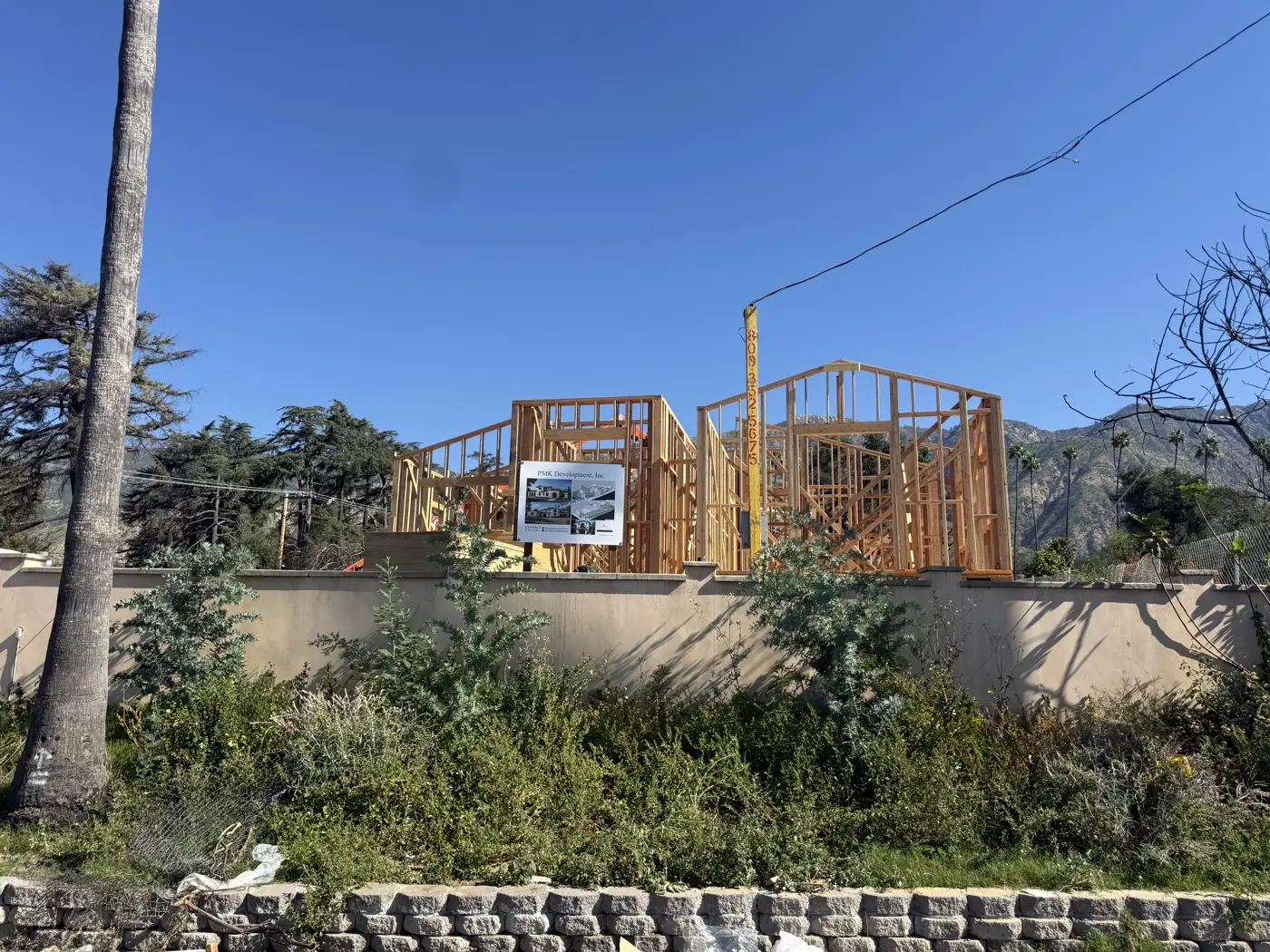 PMK Development jobsite sign in front of new home framing on Las Flores Drive in Altadena, San Gabriel foothills behind.