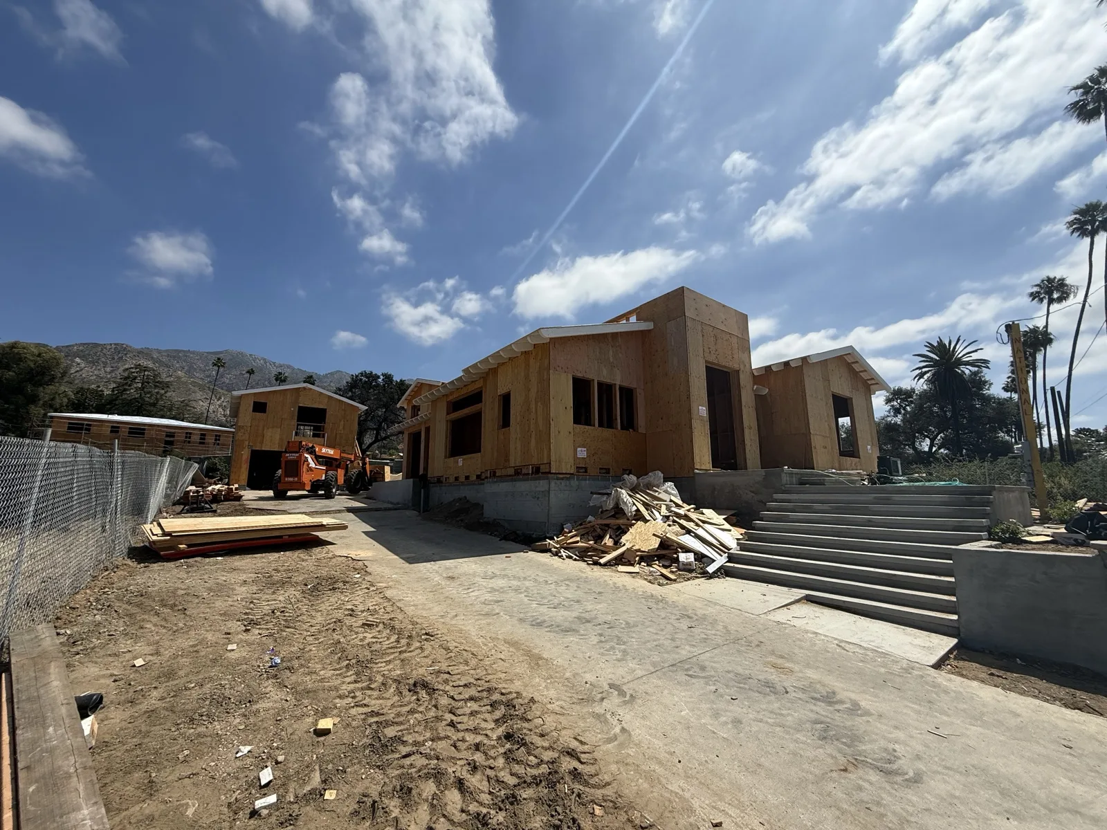 Front three-quarter view with roof framing complete and exposed rafter-tail eaves over the new concrete entry stair.