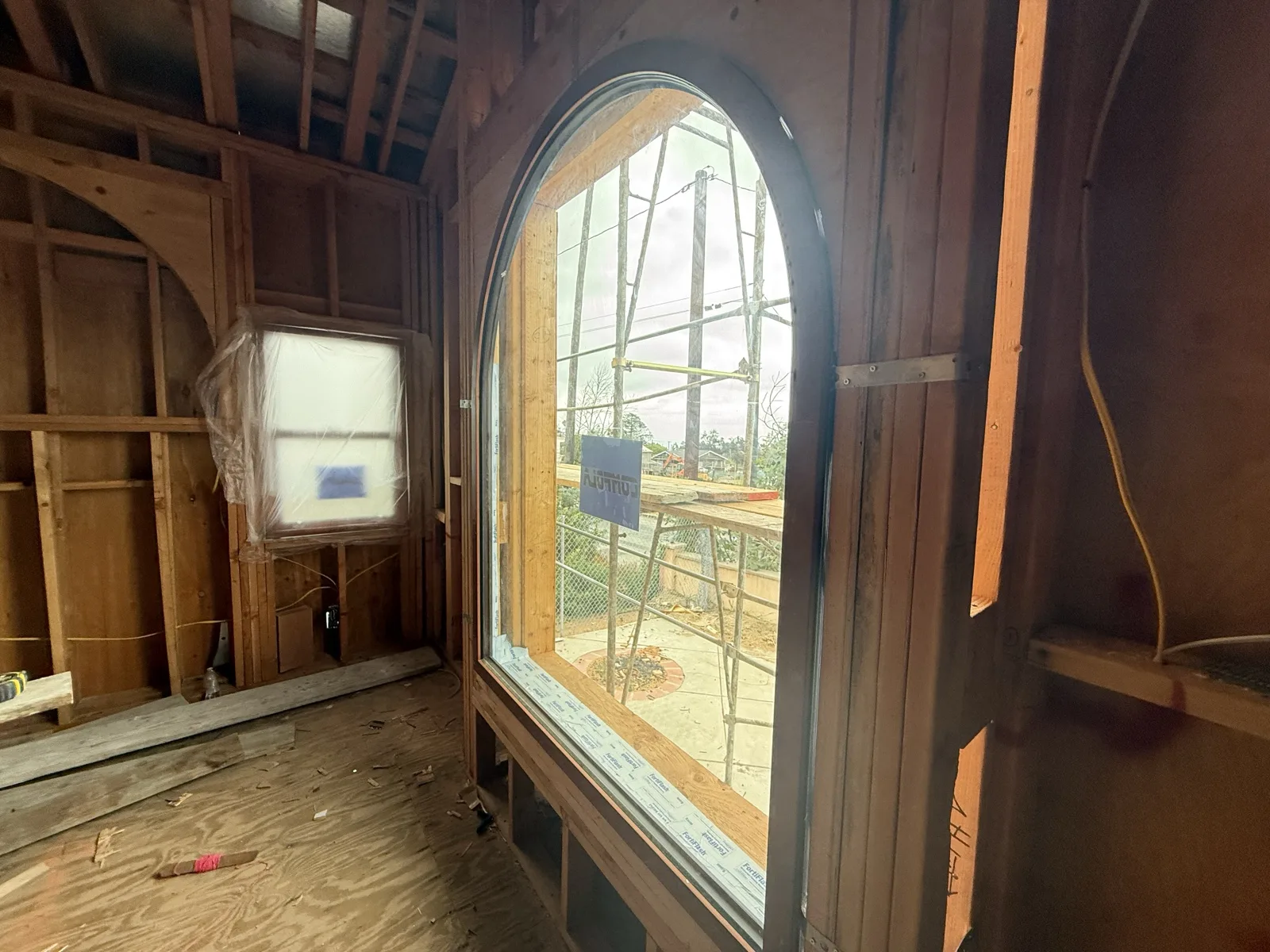 Tall arched window installed in an upstairs bedroom, with wrapped double-hung windows waiting on the subfloor.