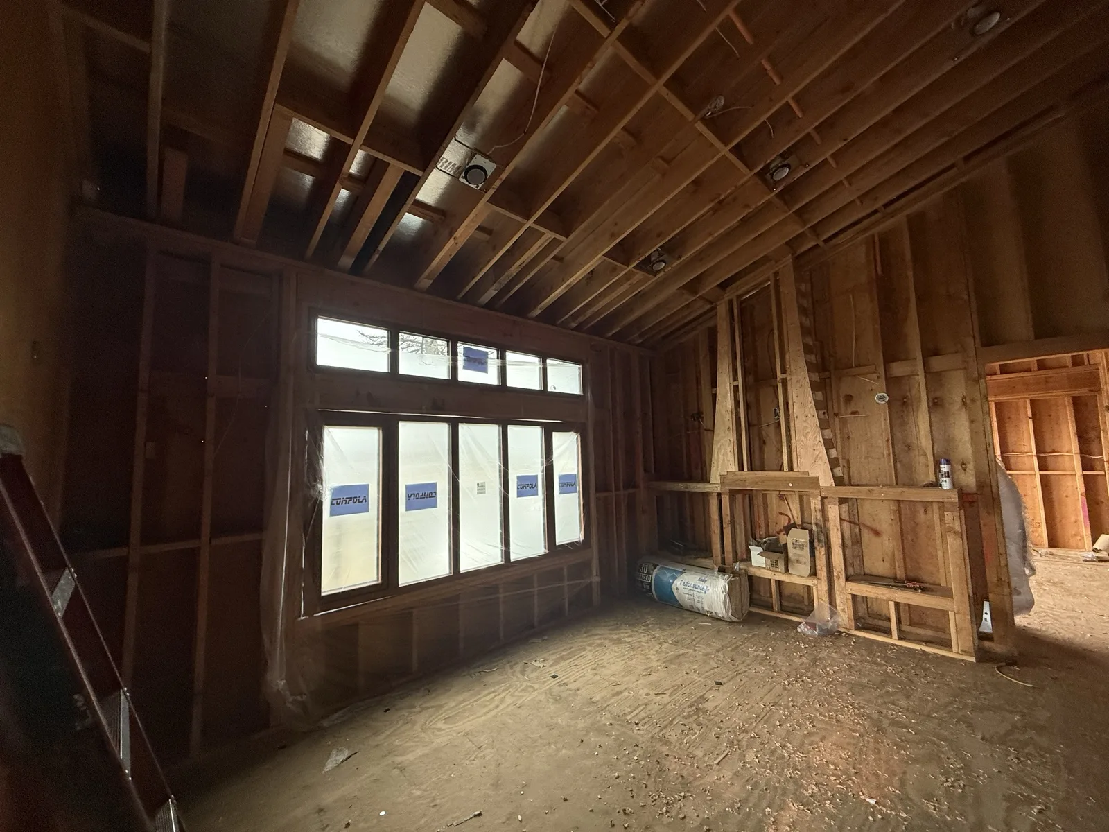 Great-room window wall installed - a wide mulled unit with transoms, recessed lights roughed into the ceiling.