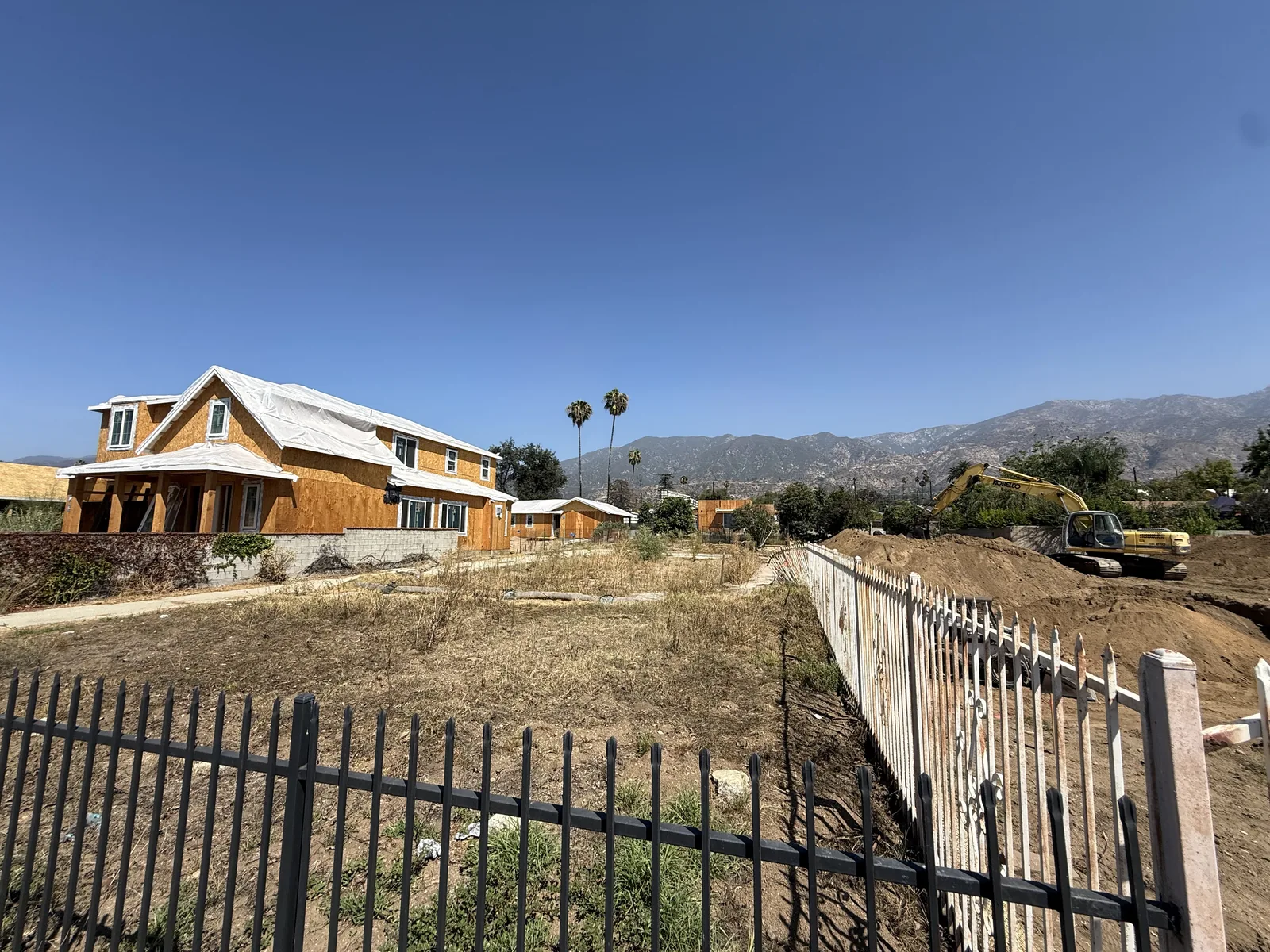 Wide view of the Mendocino lot and gate before construction, with neighboring buildings and mountains beyond