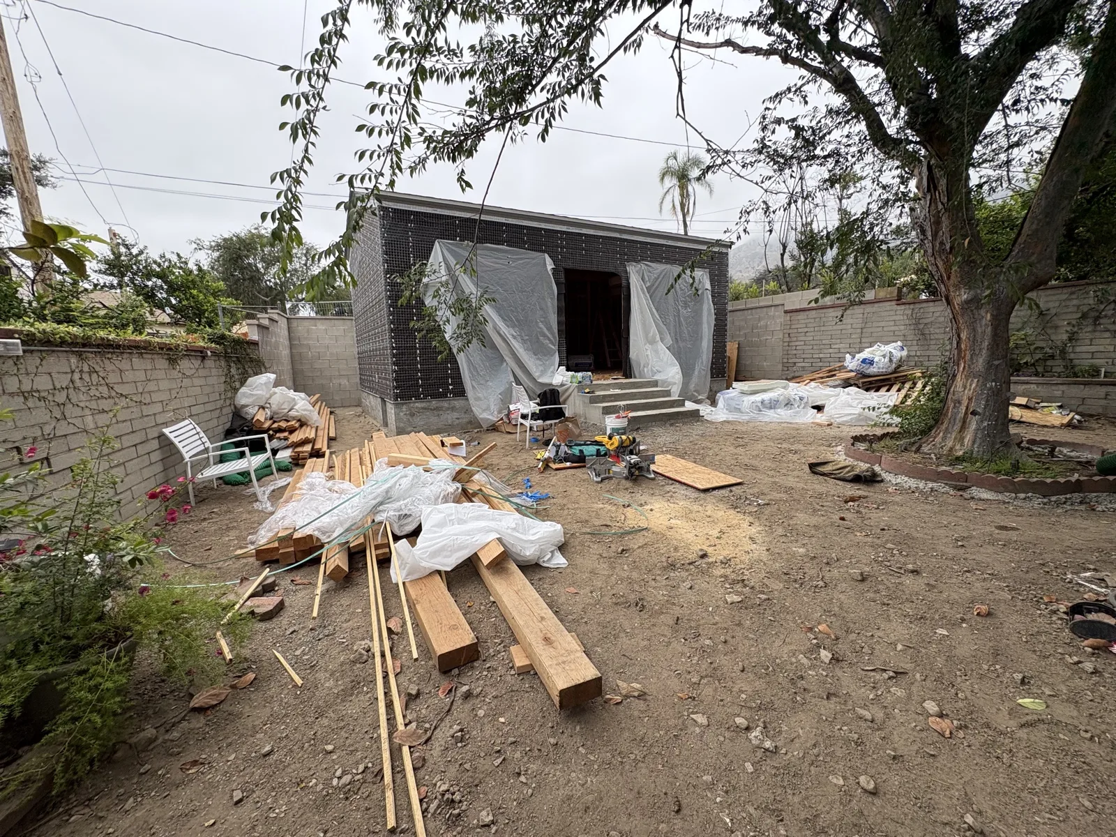 The structure wrapped in lath and paper ahead of stucco, openings masked with plastic sheeting.
