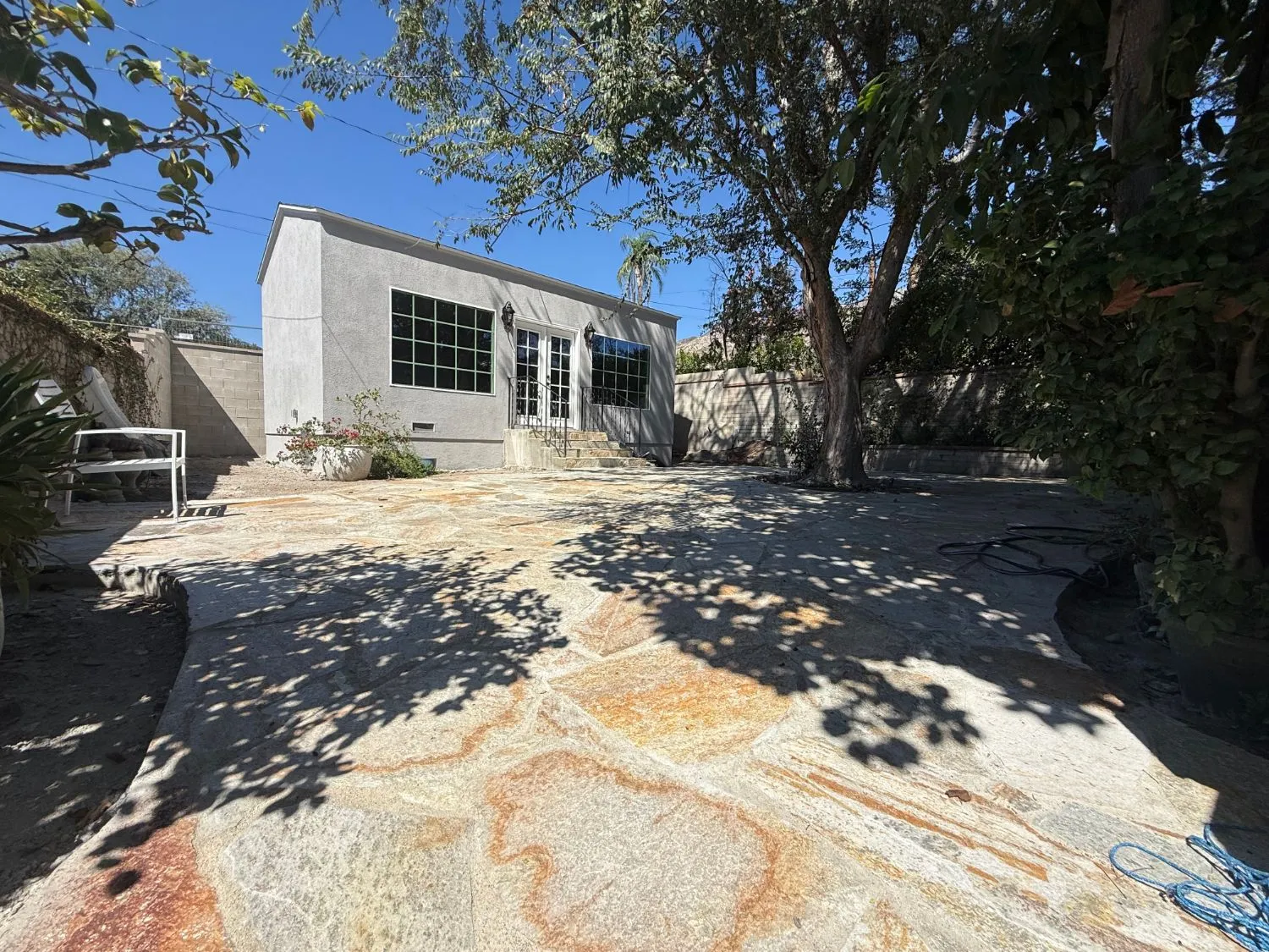 Stucco-finished detached building with French doors behind a stone patio and mature tree at PMK Development's Mt. Curve Avenue project in Altadena.
