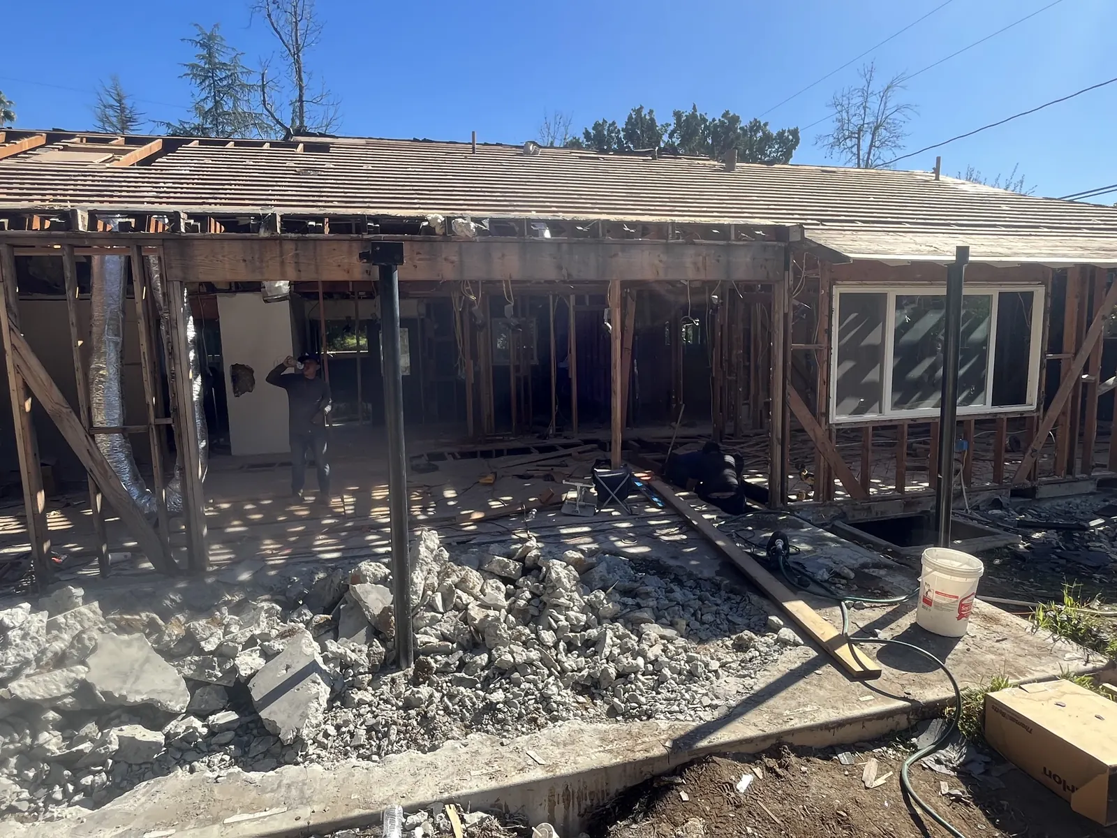 Rear of the house during demolition, with the roof stripped to sheathing, walls opened to framing, and broken concrete piled in the foreground at PMK's addition-and-renovation project in La Cañada Flintridge.
