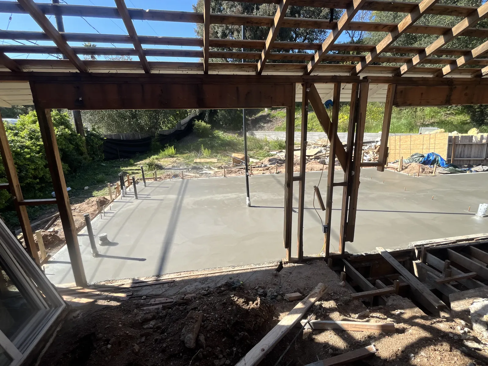 Freshly poured concrete slab with anchor bolts and plumbing stub-ups for the new addition, seen through the opened rear wall of the existing house at PMK's addition-and-renovation project in La Cañada Flintridge.