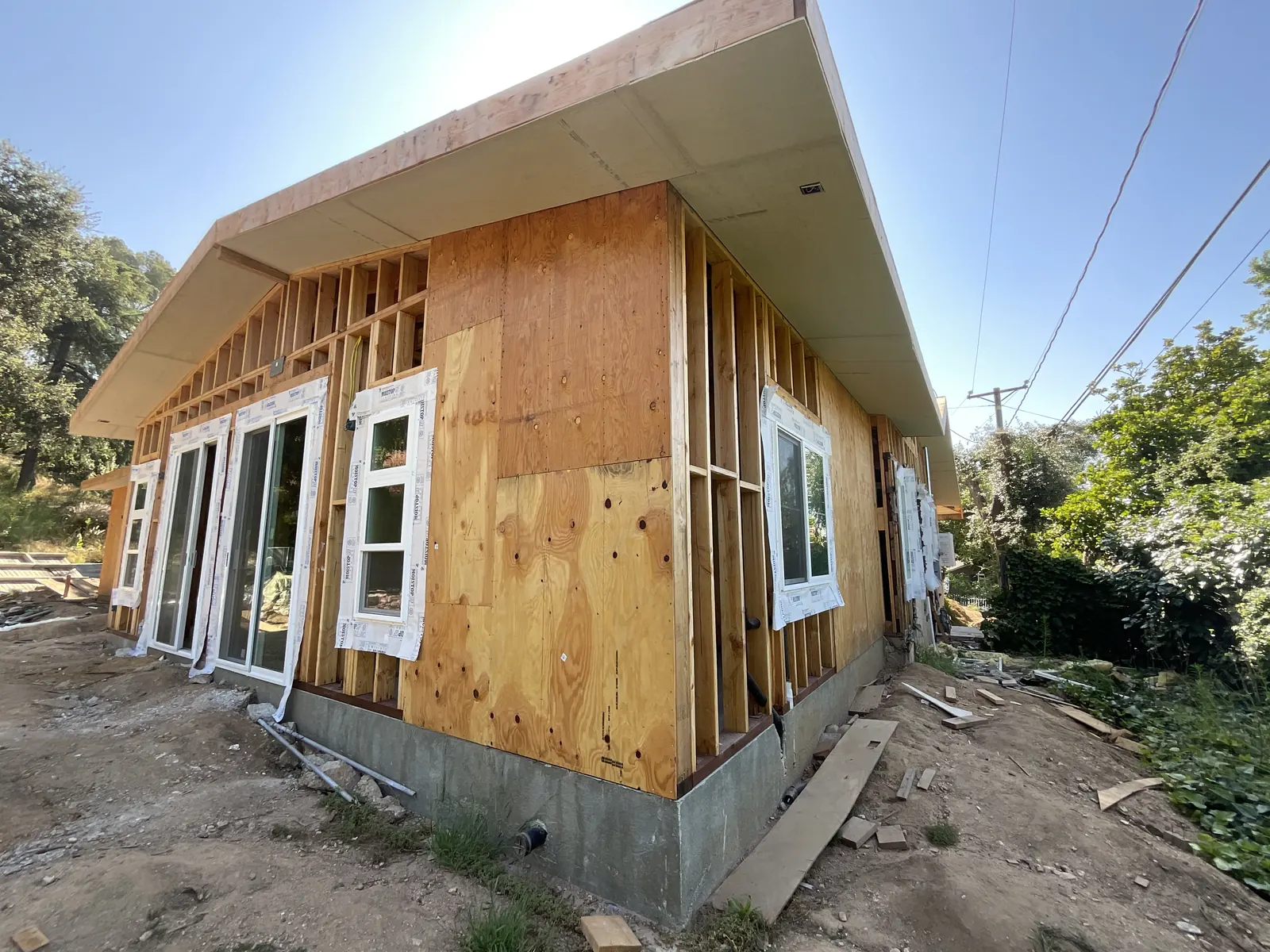 Corner of the newly framed addition wrapped in plywood sheathing, with new sliding doors and windows installed above the concrete stem wall at PMK's addition-and-renovation project in La Cañada Flintridge.